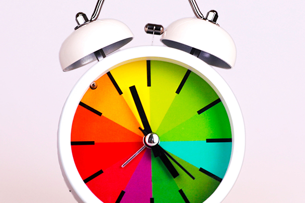 A traditional alarm clock with a bell on top and a rainbow clock face.