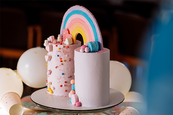 A pink celebration cake with a rainbow on top.